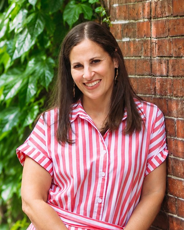Alycee Naquin smiling, standing beside a brick wall and green ivy